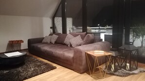 Un soggiorno moderno con un divano marrone, cuscini decorati, un piccolo tavolino in legno e un tappeto scuro.