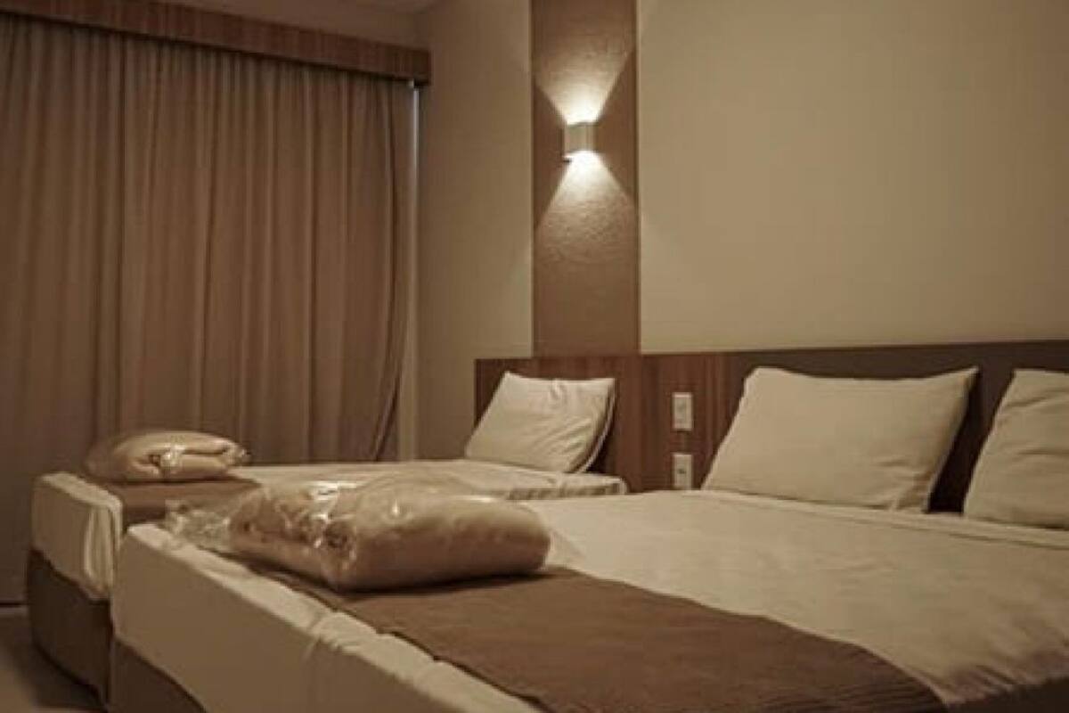 A hotel room with two beds, a nightstand, and a wall-mounted light.
