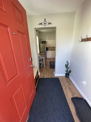 A hallway leading to a kitchen with white cabinets, a red door, and a small potted plant.