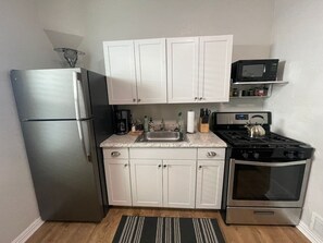 A compact kitchen with a refrigerator, stove, oven, and white cabinets.