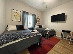 A hotel room with two beds, a TV, a desk, and a red carpet.