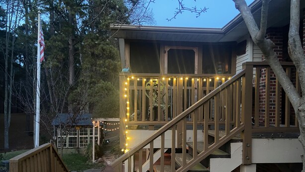 A wooden deck with a staircase leading to a covered area with string lights.