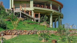 A large, single-story building with a curved roof, situated on a grassy hill.