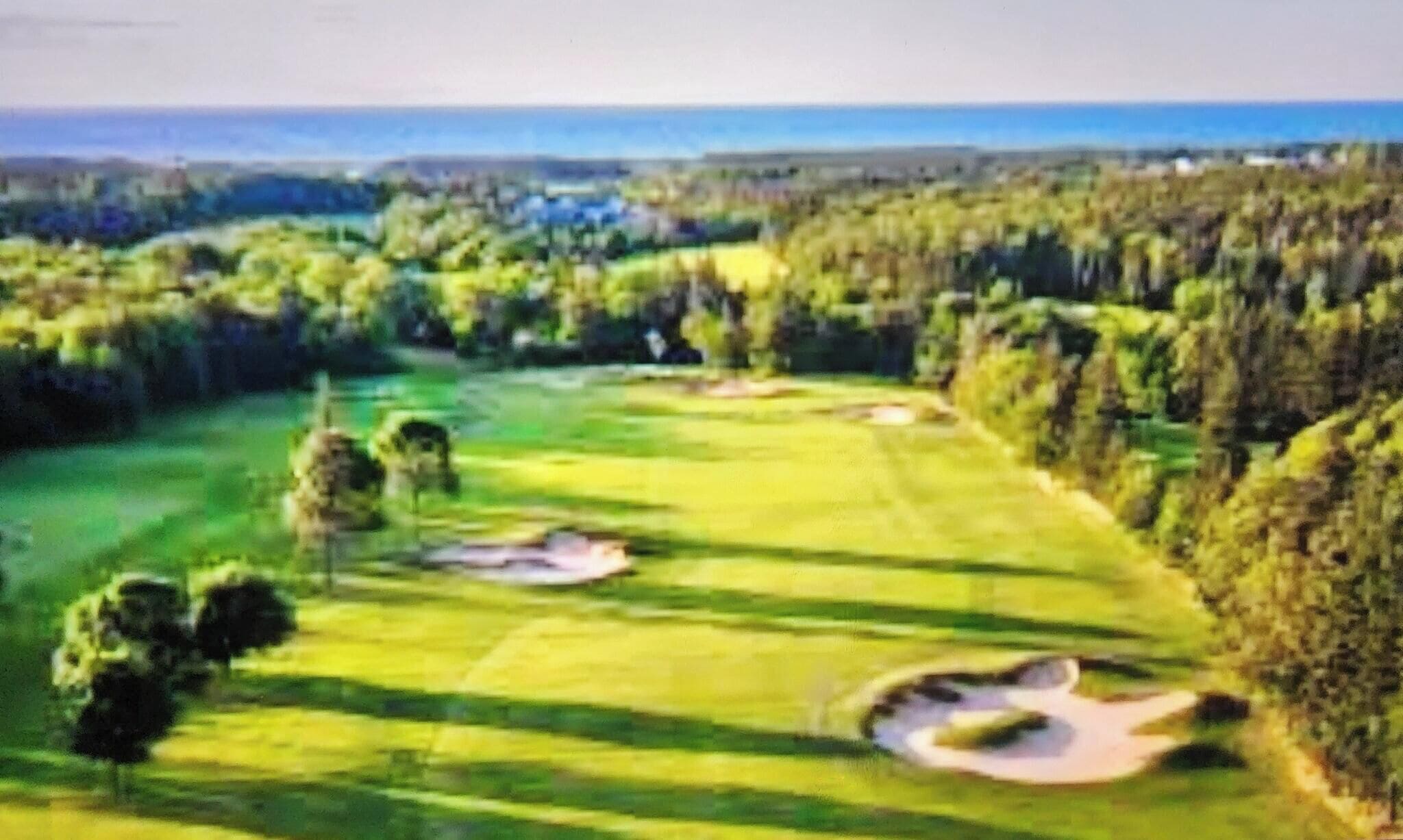 A golf course with sand bunkers, trees, and a view of the ocean.