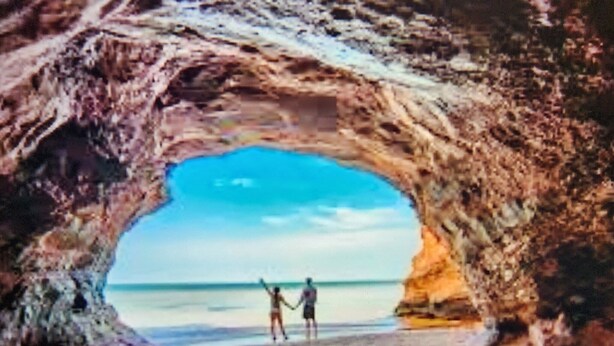 Une scène de plage avec une arche naturelle formée par des rochers.