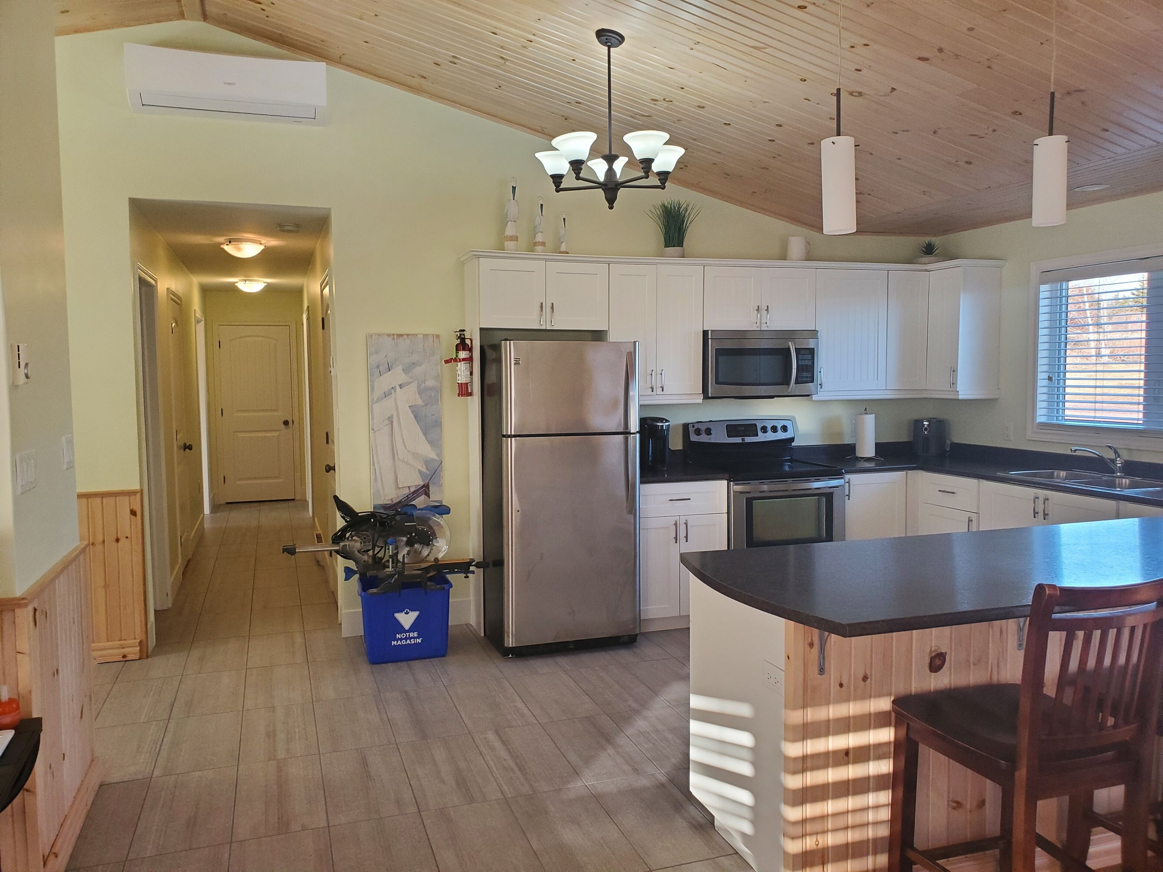 A modern kitchen with white cabinets, stainless steel appliances, and a wooden ceiling.