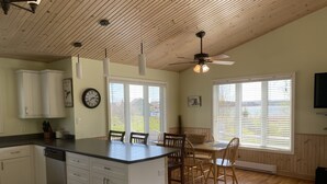 Une cuisine avec un plafond en bois, des armoires blanches, un îlot central et un coin repas avec des chaises et une table en bois.