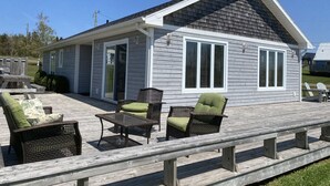 Une maison de plain-pied dotée d’un patio couvert aménagé avec des meubles en osier et une table à plateau en verre.