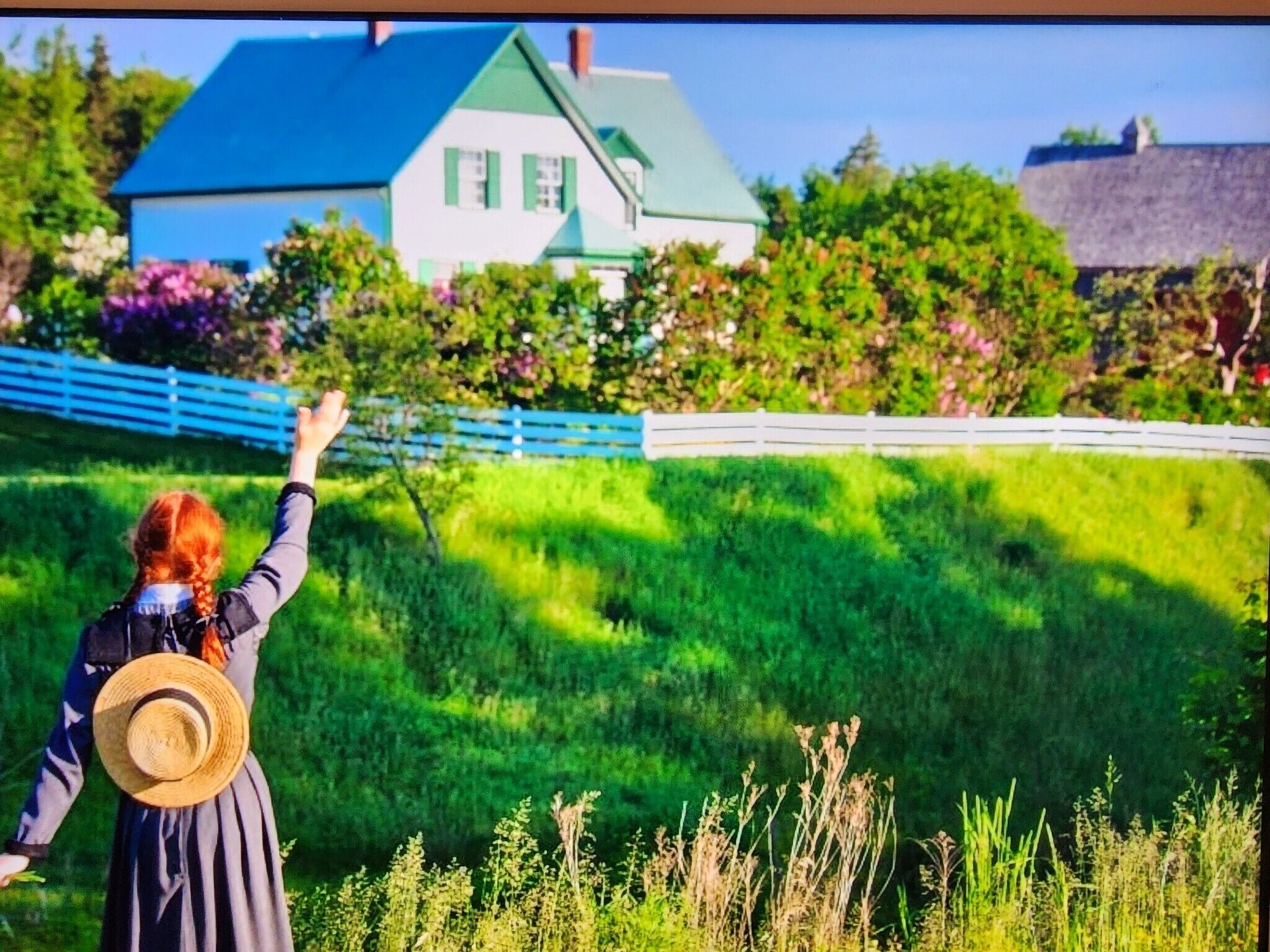 A person with a straw hat standing in a grassy area with a house in the background.