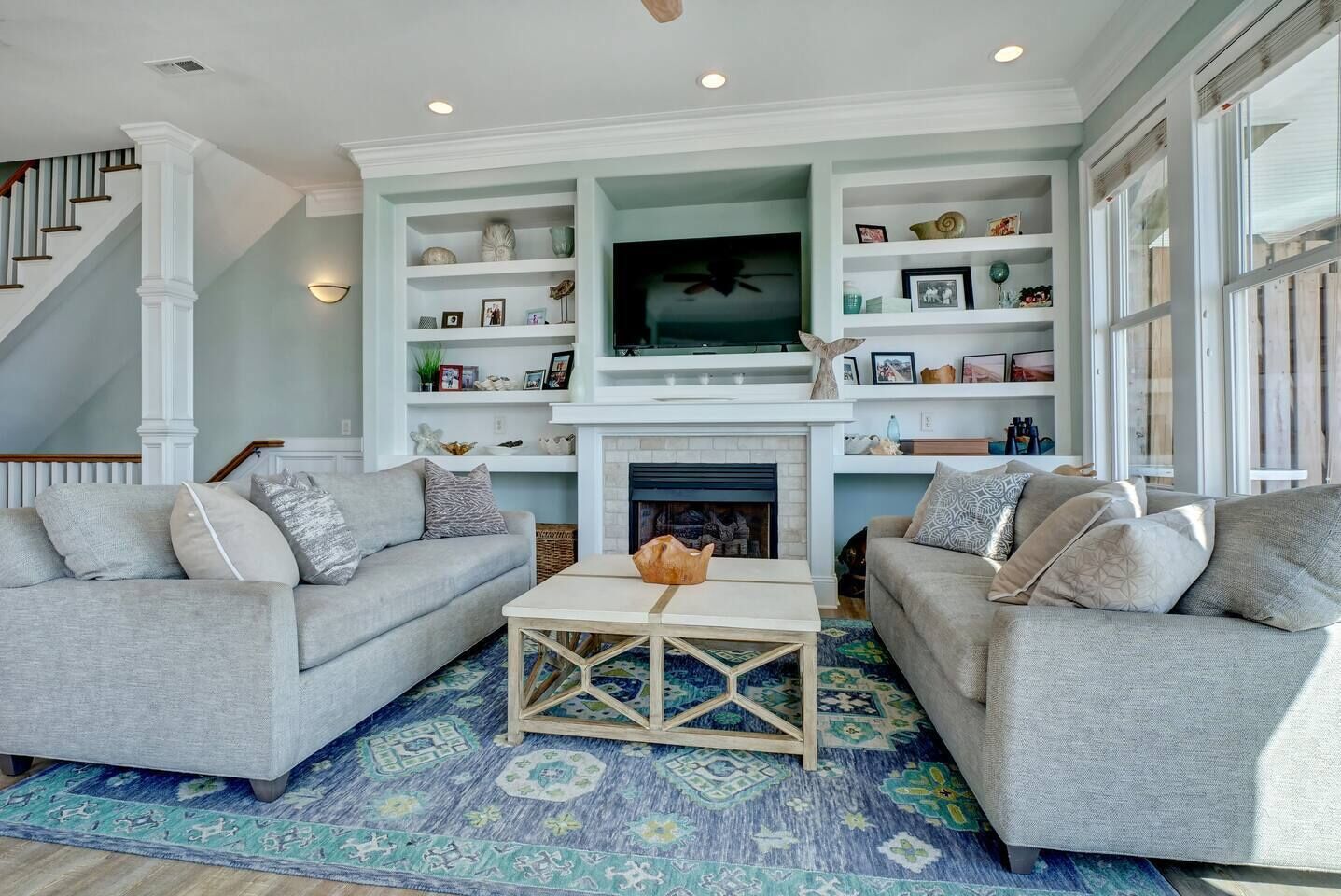 A living room with two grey sofas, a coffee table, and a fireplace. There are shelves above the fireplace with various decorative items.