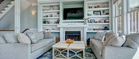 A living room with two grey sofas, a coffee table, and a fireplace. There are shelves above the fireplace with various decorative items.