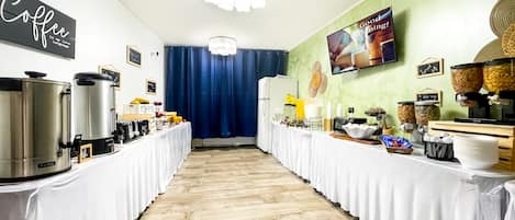 Buffet med kaffemaskiner og cornflakes-dispensere, et fjernsyn og et skilt med teksten "Good Morning!".