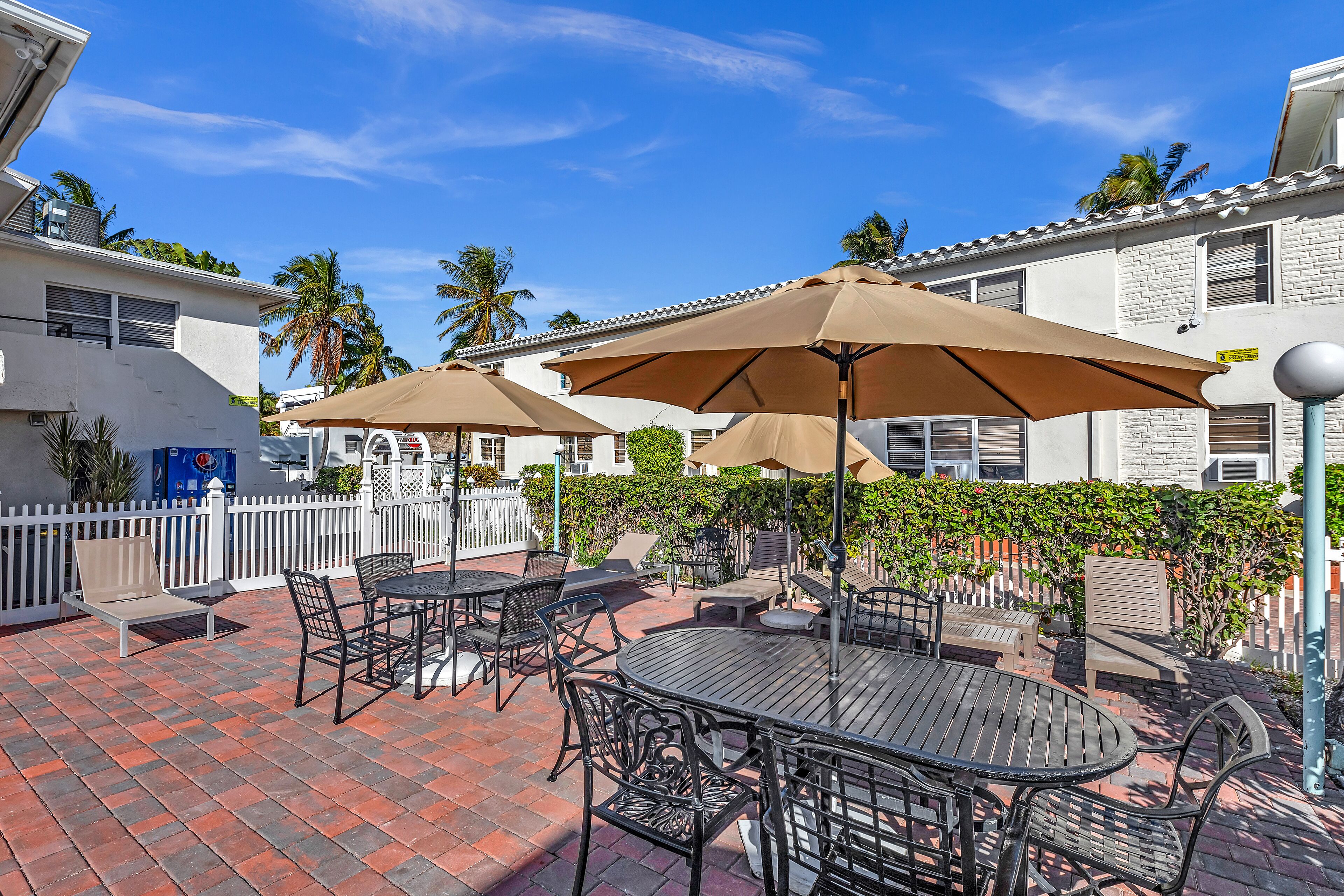 An outdoor patio with tables and chairs, umbrellas, and a white fence.