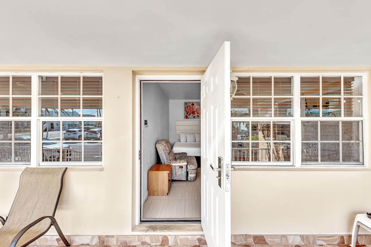 A room with a large window, a chair, a small table, and a door leading to another room.