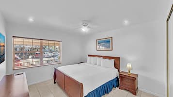 A bedroom with a bed, a nightstand, a ceiling fan, a window with blinds, and a painting on the wall.
