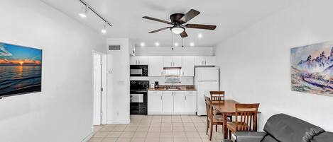 A modern kitchen with white cabinets, a dining area with a wooden table and chairs, and a grey sofa.