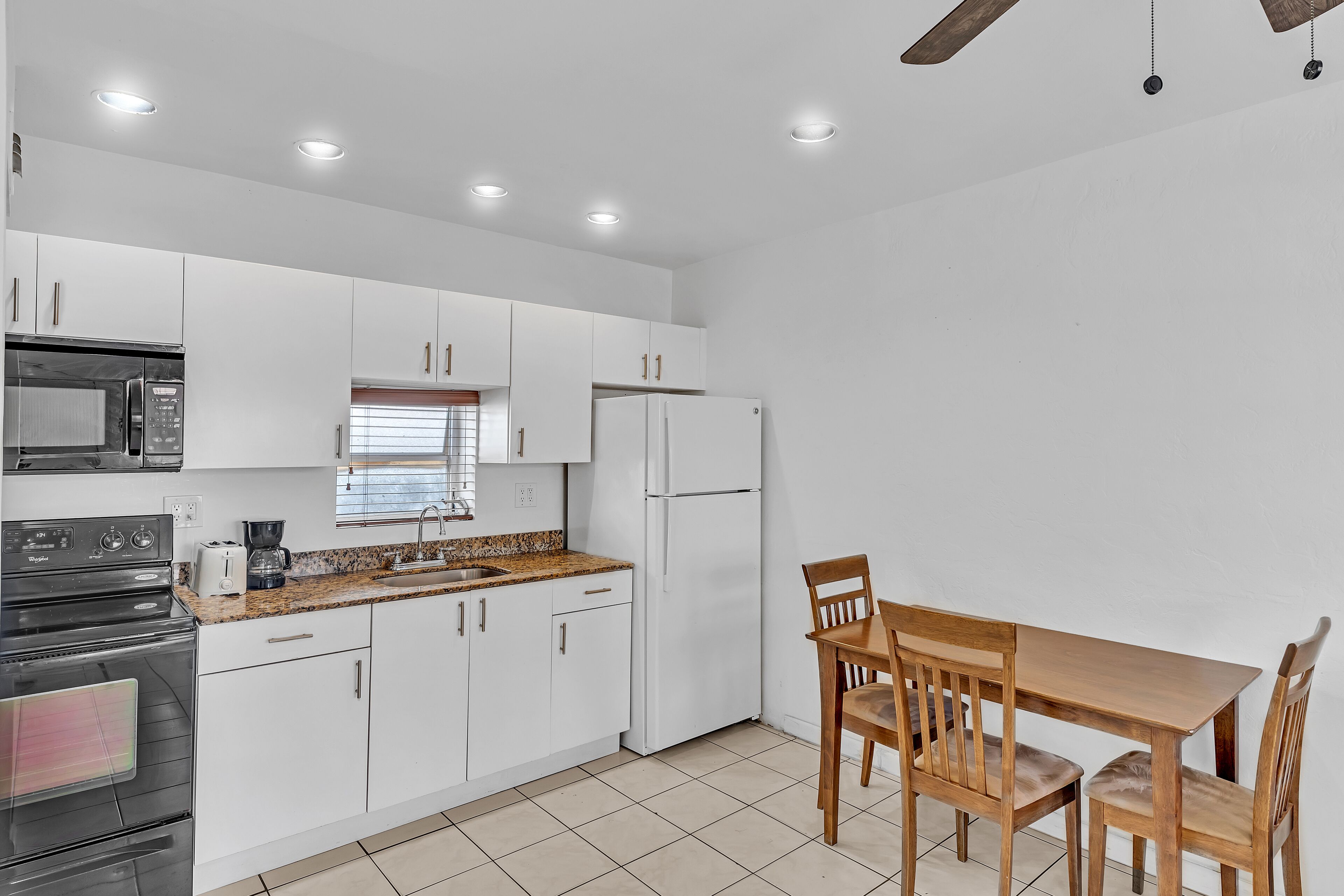 A modern kitchen with white cabinets, a stainless steel stove, a refrigerator, and a wooden dining table with chairs.