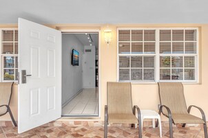 An open door leading to a hallway with a tiled floor, a wall-mounted TV, and a window with blinds.
