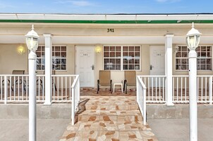 A building with a numbered address, a tiled entrance, and a seating area with chairs and tables.
