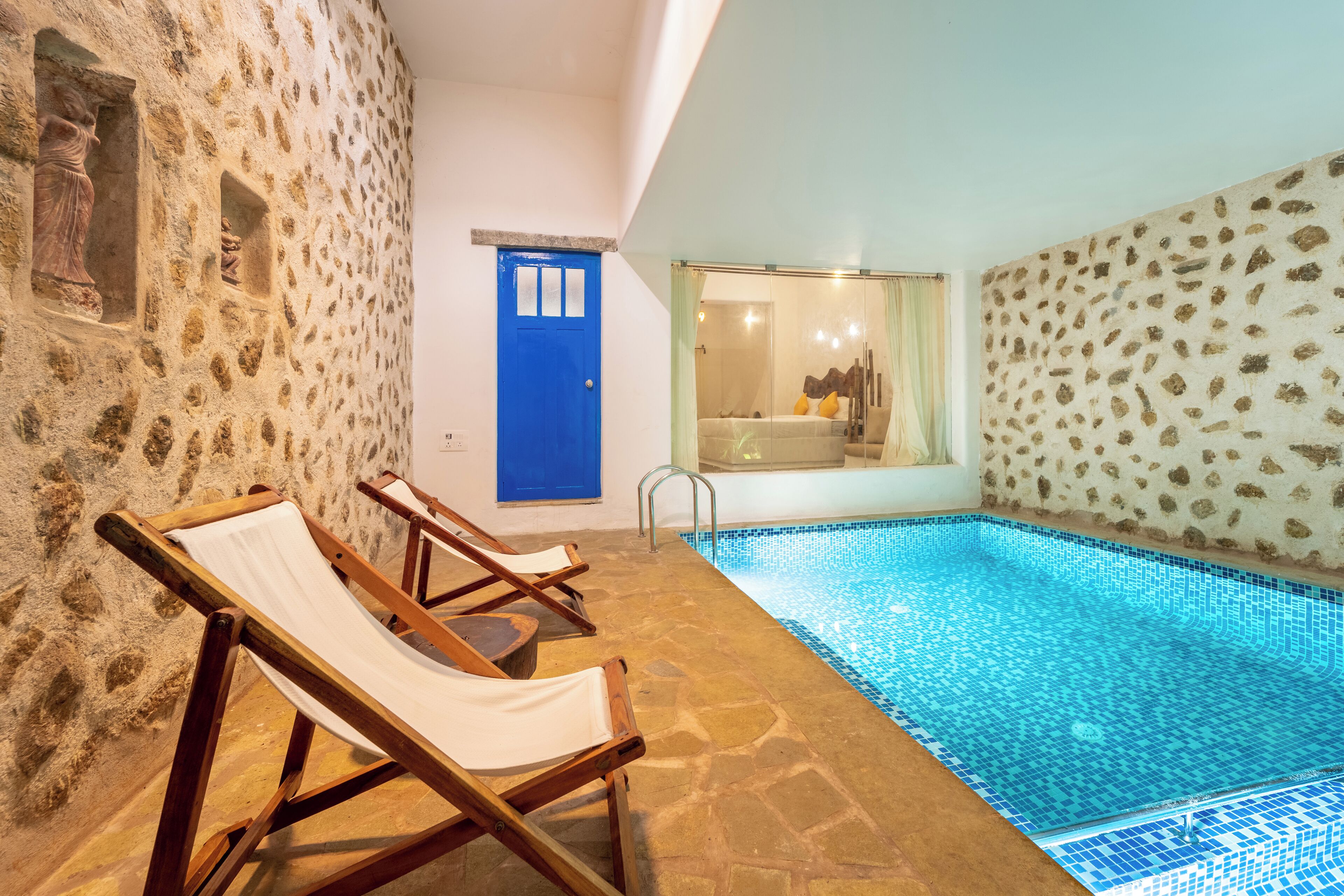 A pool area with stone walls, a blue door, and lounge chairs.