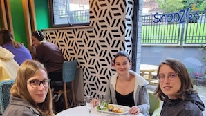 Un groupe de personnes est assis autour d’une table ronde, devant un mur décoré et avec vue sur l’extérieur.