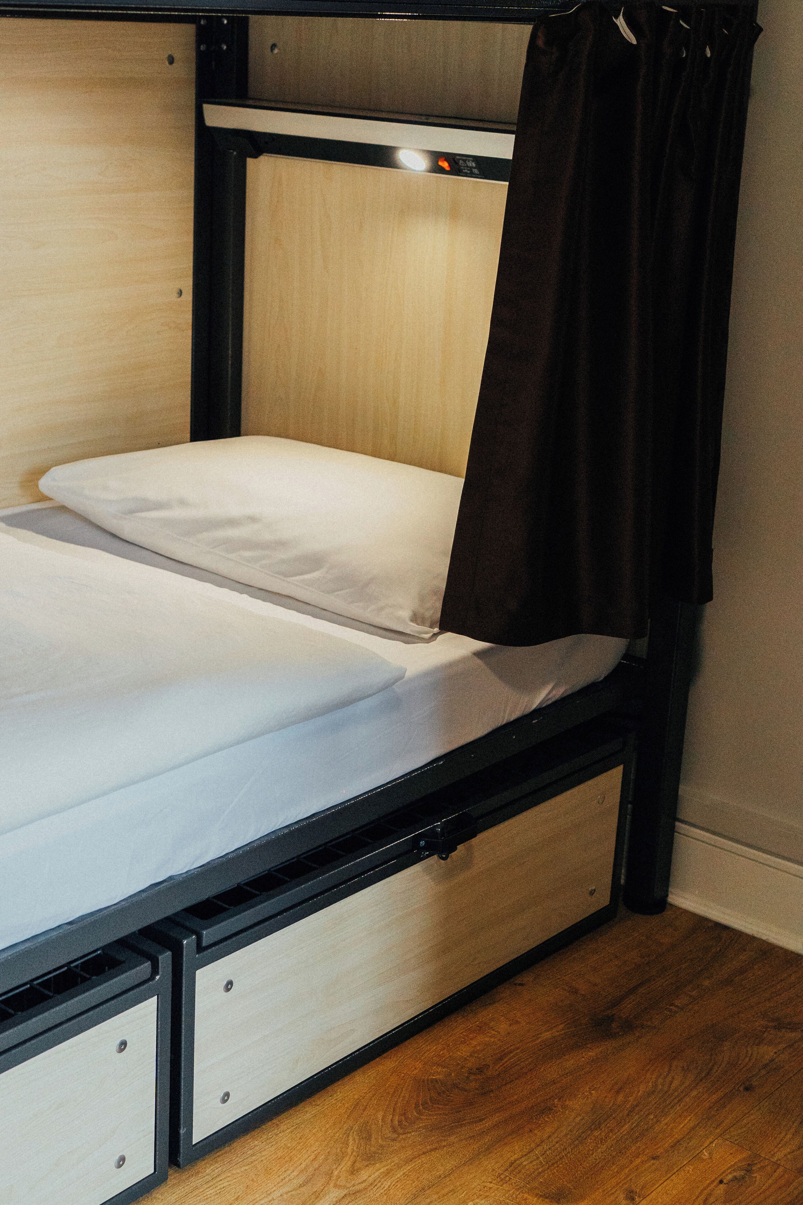 Un lit superposé avec une tête de lit en bois, un matelas blanc et un rideau noir.