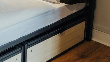 Un lit superposé avec une tête de lit en bois, un matelas blanc et un rideau noir.