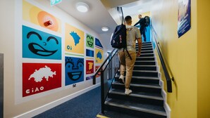 Un escalier orné d’œuvres d’art murales aux couleurs vives, avec une main courante, et une personne qui descend.