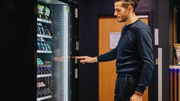 A person interacting with a vending machine in a room with a wooden door and a sign on the wall.