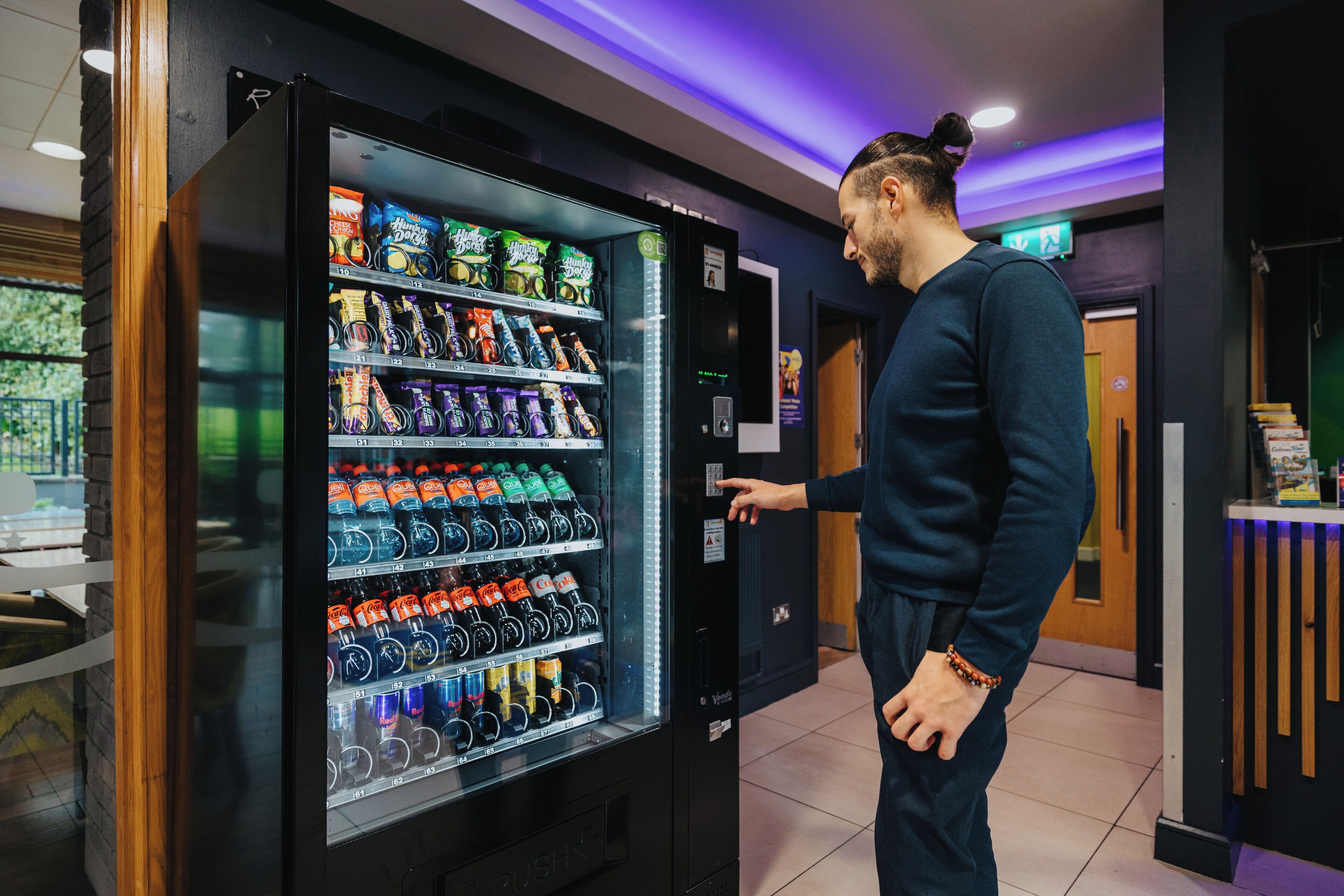 A man interacting with a vending machine stocked with various beverages and snacks.