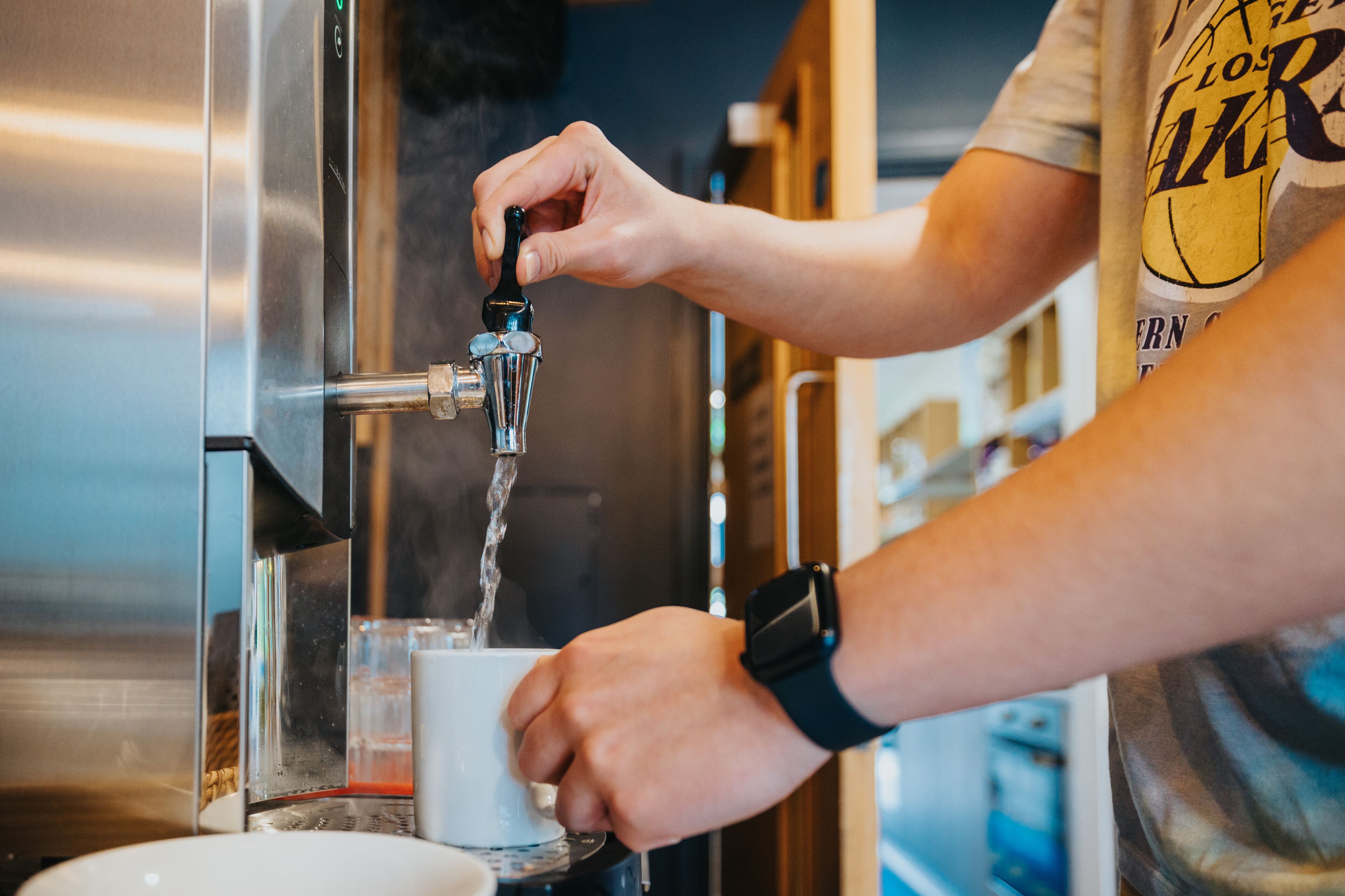 A person operating a coffee machine, dispensing water into a cup.