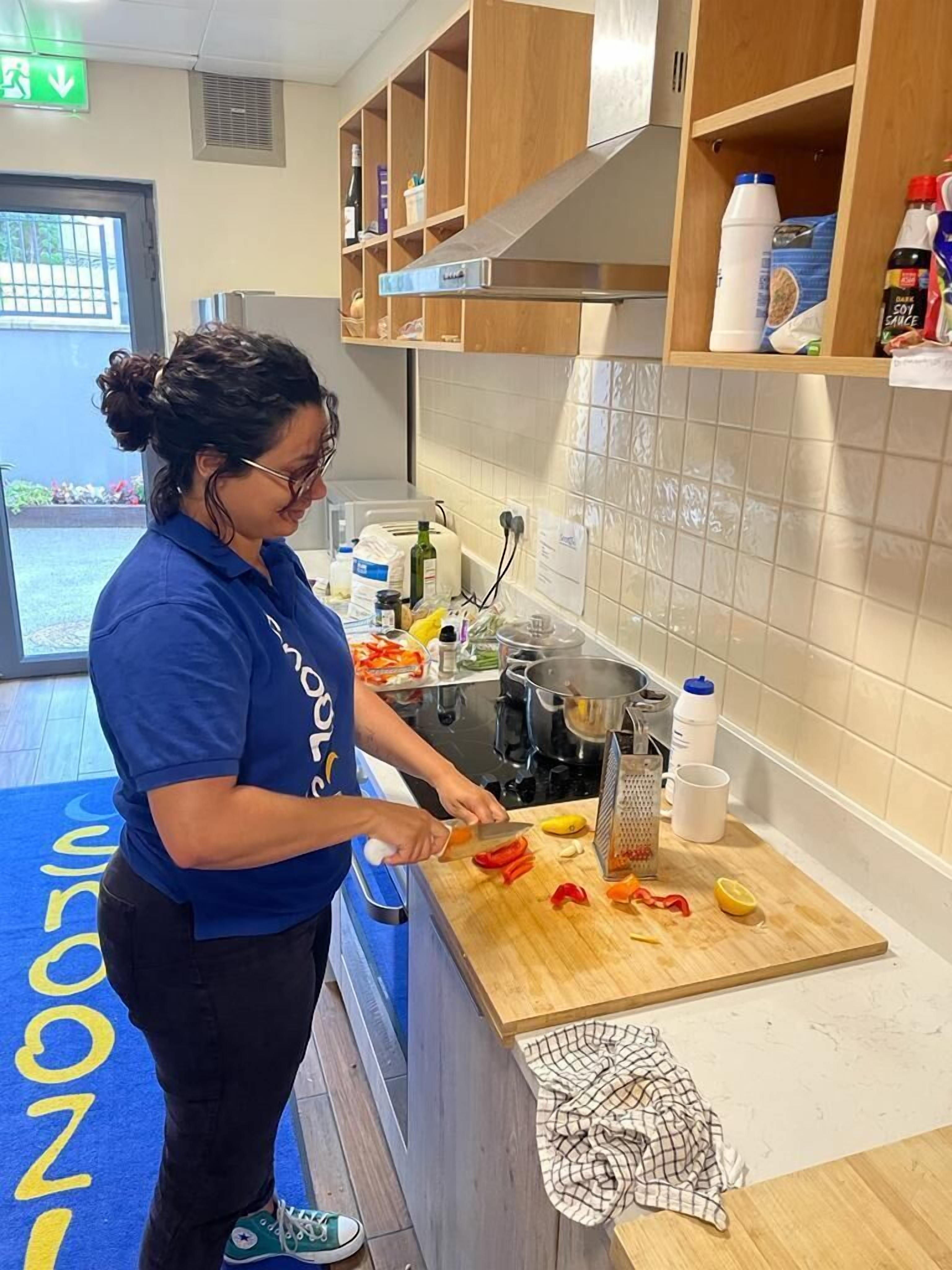Una persona preparando comida en una cocina con armarios de madera, un respuesto de azulejos y un tapete azul en el suelo.