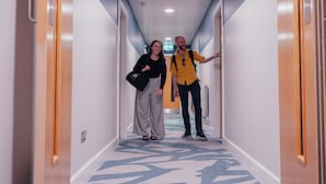 Un couloir d’hôtel avec un tapis à motifs, des portes en bois et une décoration aux couleurs bleu et blanc.