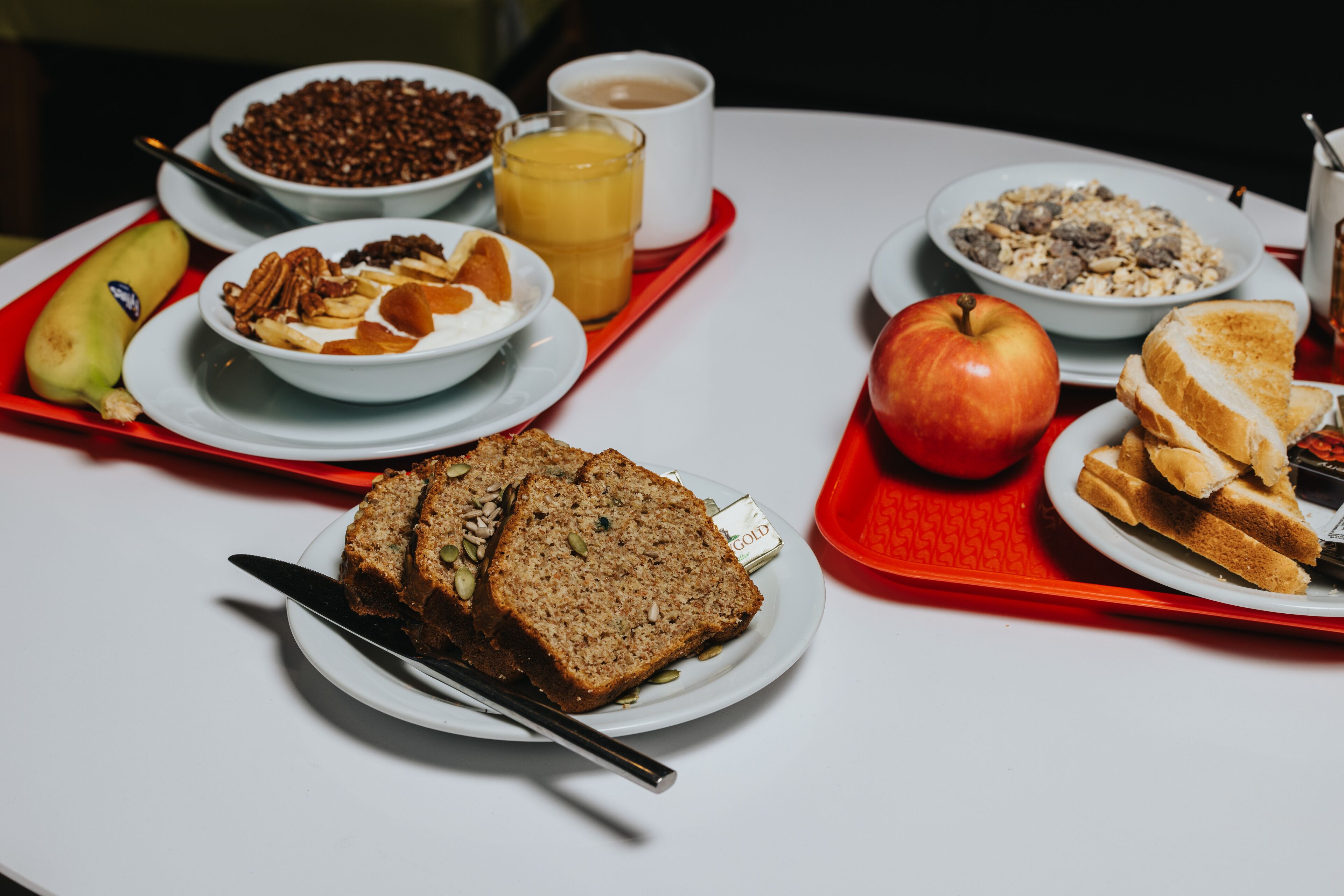 A breakfast tray with various food items including bread, an apple, a banana, and a bowl of cereal.