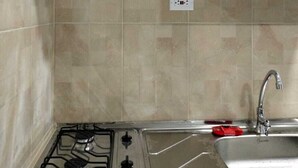 Uma cozinha com fogão a gás, pia e prateleira sobre o fogão com um liquidificador, uma chaleira e uma panela vermelha.