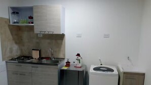 Uma cozinha compacta com fogão a gás, pia, pequena geladeira e micro-ondas.