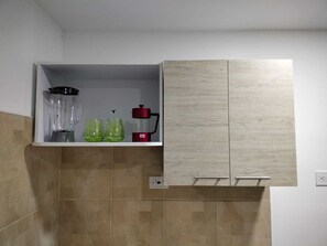 Cocina con un estante empotrado que contiene una licuadora, dos vasos verdes y una cafetera roja.