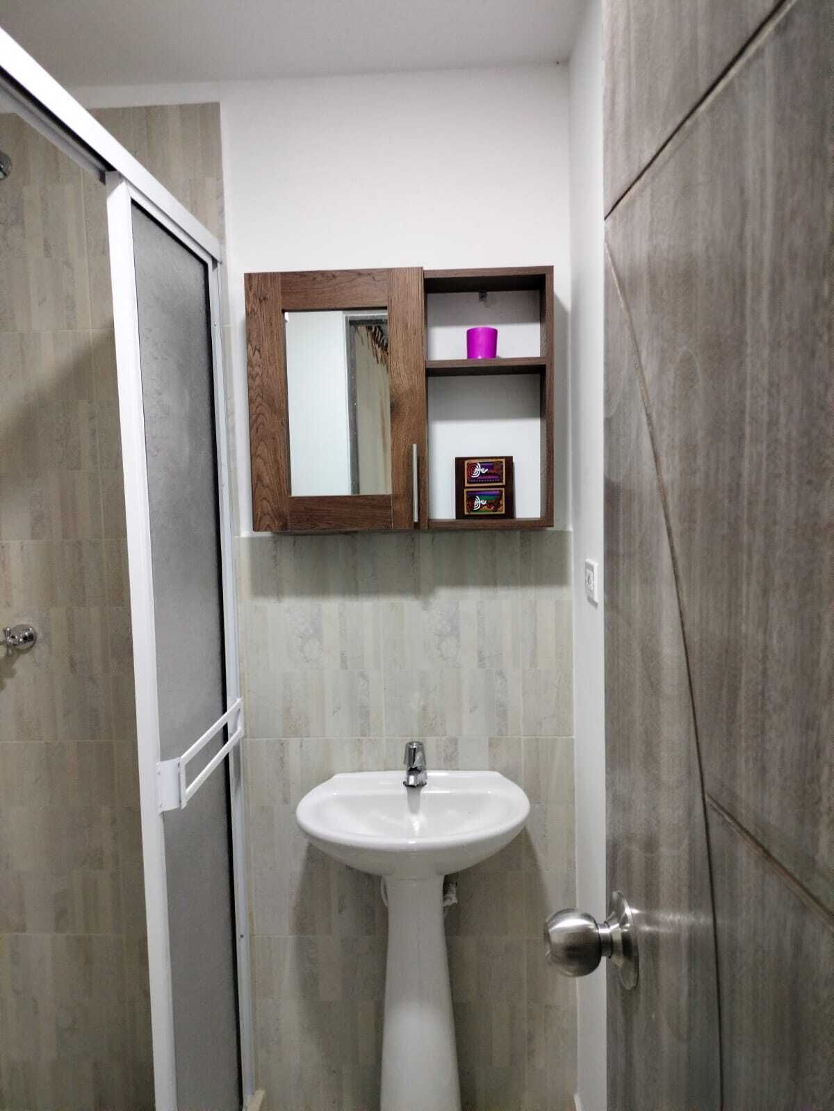A bathroom with a white pedestal sink, a wooden medicine cabinet, and a door with a sliding mirror.