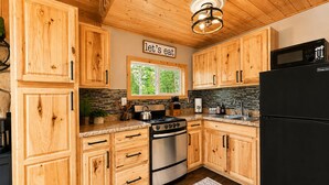 A kitchen with wooden cabinets, a stove, a refrigerator, and a window with a view of greenery.