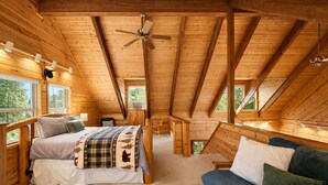 A cozy attic bedroom with a bed, a blue sofa, a wooden coffee table, and a ceiling fan.