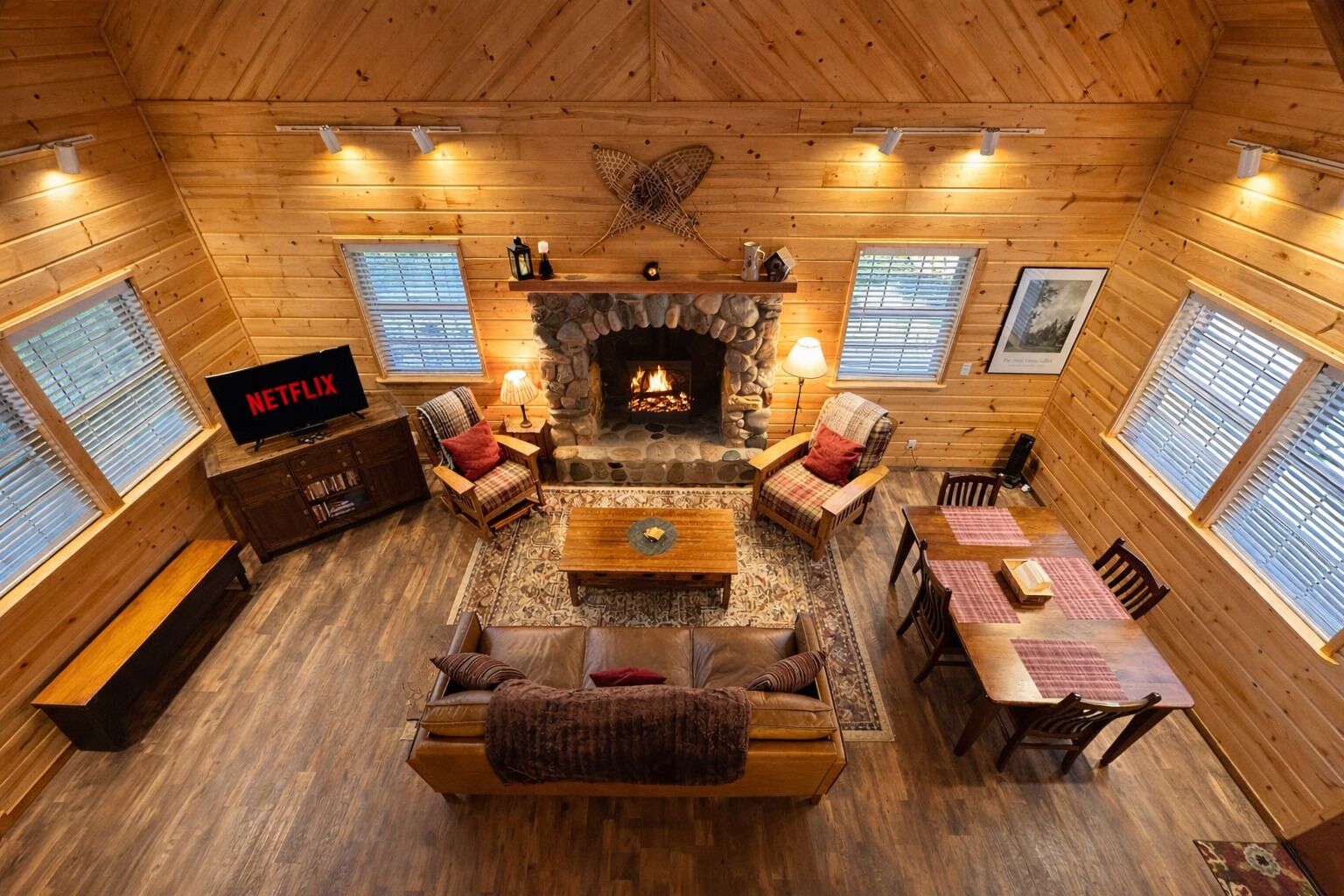A cozy cabin interior with a stone fireplace, wooden walls, a television, and a dining area.