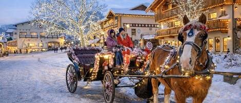 Une calèche tirée par des chevaux, transportant des passagers, entourée de neige et bordée de bâtiments illuminés.