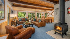 A cozy living room with leather sofas, a fireplace, and large windows offering a view of the outdoors. - Chiwawa River Chalet 3 Bedroom Home by NW Comfy Cabins by RedAwning (Leavenworth)