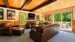 A cozy living room with a leather sofa, a television, and a large window overlooking a deck. - Chiwawa River Chalet 3 Bedroom Home by NW Comfy Cabins by RedAwning (Leavenworth)