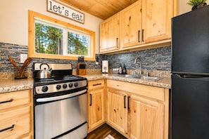 Une cuisine avec des meubles en bois, une cuisinière en acier inoxydable, un réfrigérateur noir et une fenêtre donnant sur les arbres.