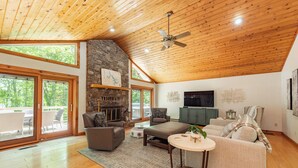 A spacious living room with a stone fireplace, wooden ceiling, and large windows. - Lakefront Dog Friendly Cottage w/ Dock & Fire Pit (Swanton)