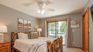 A bedroom with a wooden bed, a ceiling fan, and a large window with curtains. - Lakefront Dog Friendly Cottage w/ Dock & Fire Pit (Swanton)