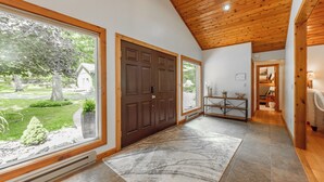 A spacious hallway with a wooden ceiling, large windows, and a stone-tiled floor. - Lakefront Dog Friendly Cottage w/ Dock & Fire Pit (Swanton)