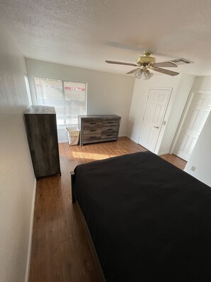 Cozy retreat with a large bed, dresser, and table, set against a serene backdrop.