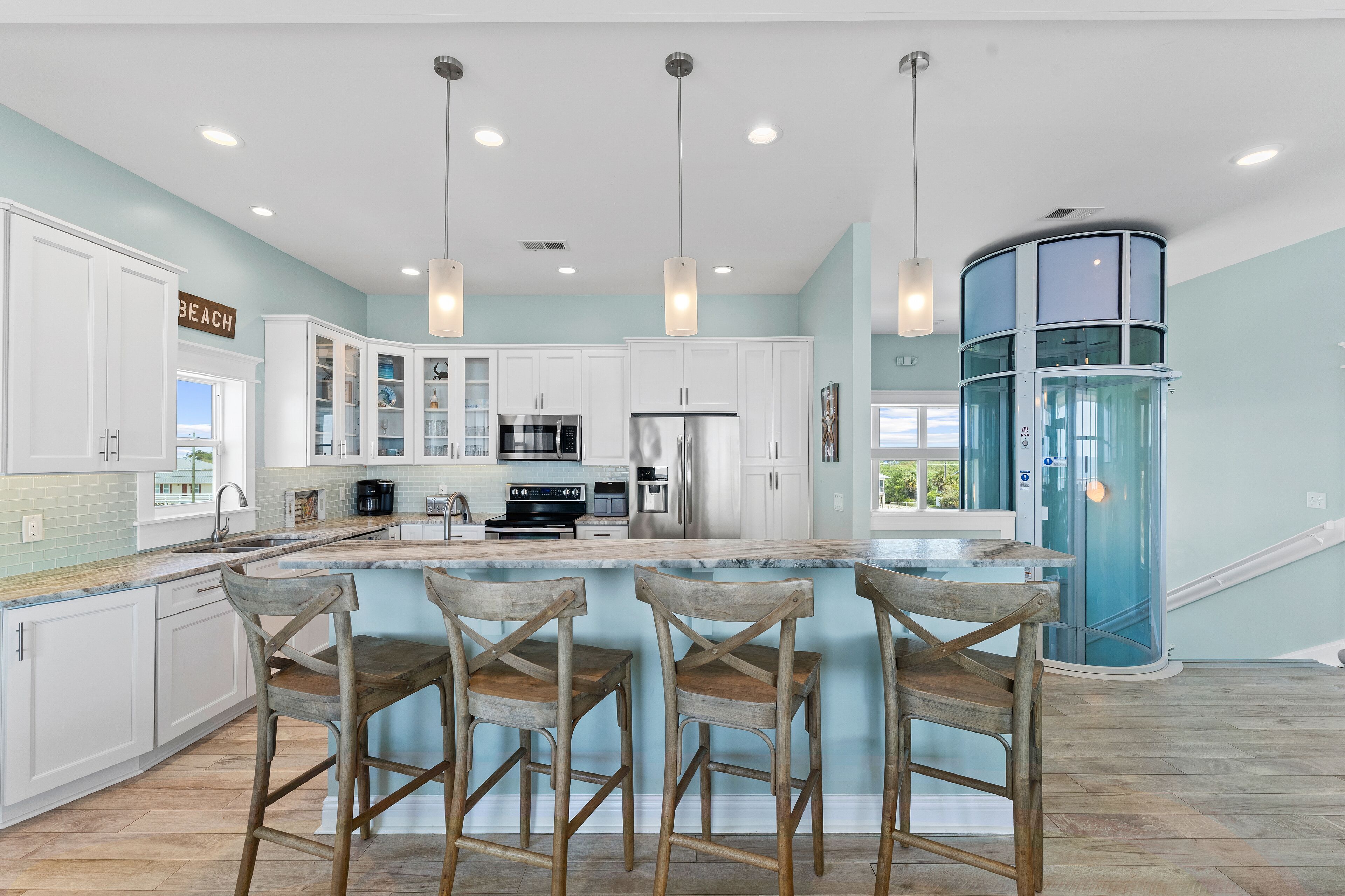 A modern kitchen with white cabinets, a central island with bar stools, stainless steel appliances, and pendant lighting.
